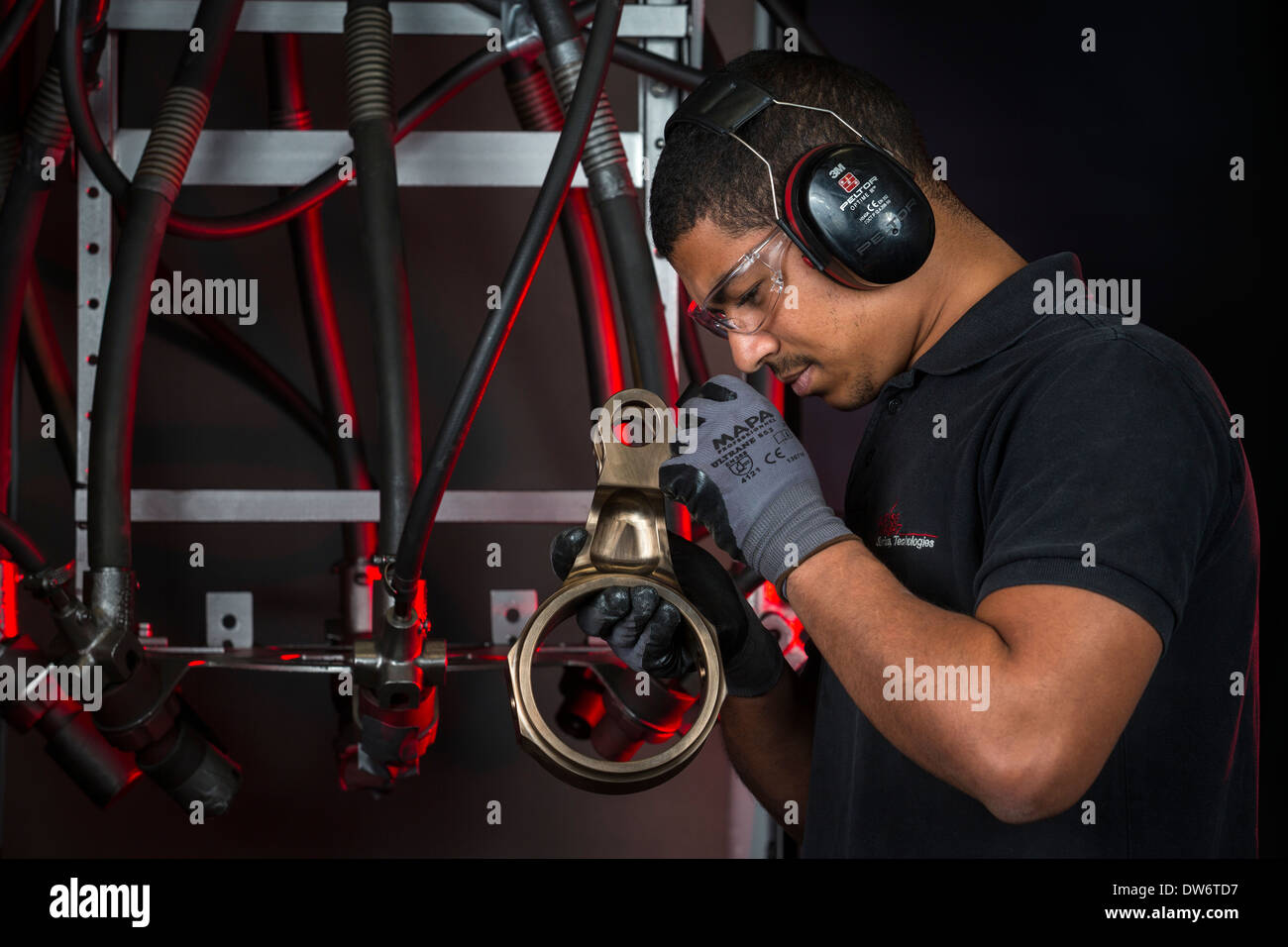 Ein Operator einen Ersatz vor seinem Strahlanlage genauer unter die Lupe nehmen. Opérateur Examinant Une Pièce Mécanique. Stockfoto