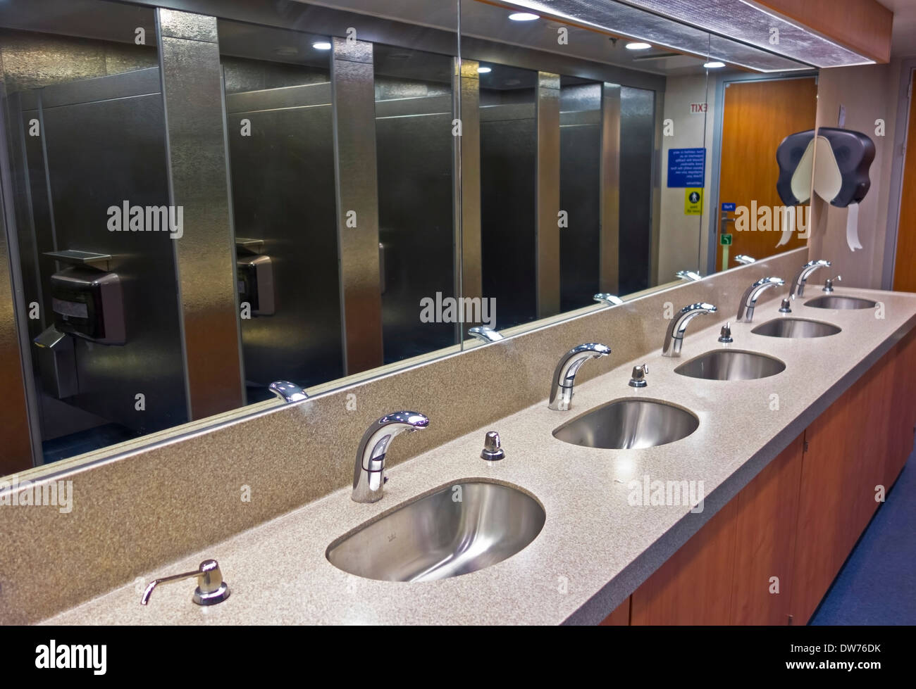 Eine Reihe von Waschbecken und Metallständen, die sich in den Spiegeln eines Fährschiffes spiegeln. Automatische Wasserhähne für mehr Sauberkeit. Stockfoto