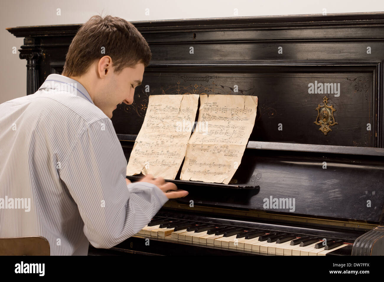 Ansicht von hinten von einem jungen Mann lächelnd, als er mit einem alten Vintage Filmmusik auf einem aufrechten hölzernen Klavier Klavier spielt Stockfoto