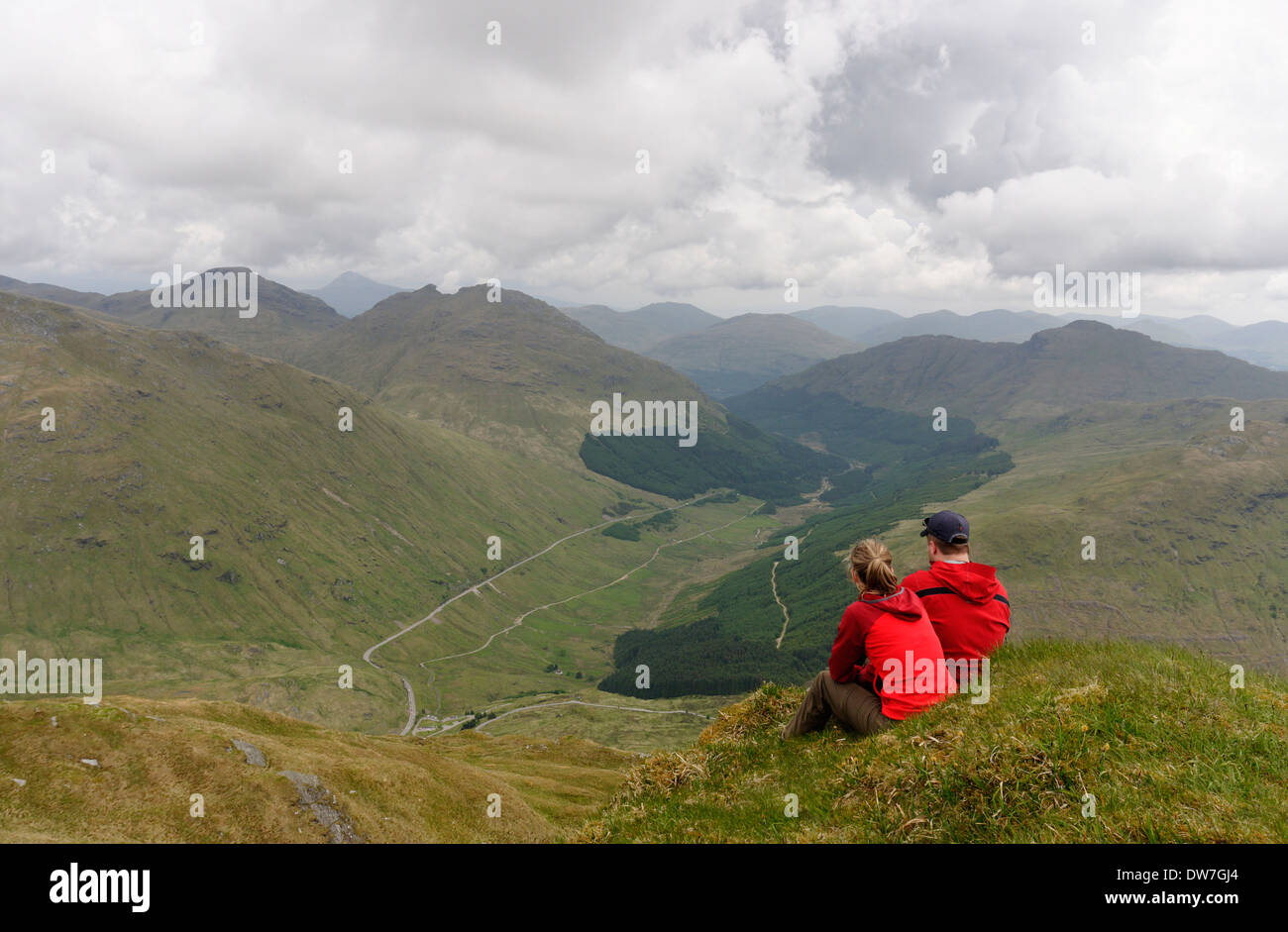 Ein junges Paar saß auf einem Berggipfel in den schottischen Highlands rot gekleidet Stockfoto