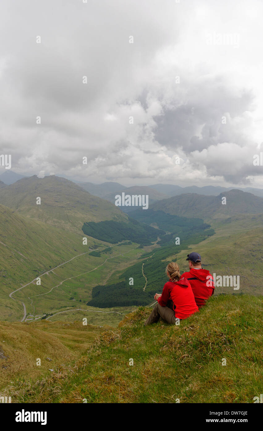 Ein junges Paar saß auf einem Berggipfel in den schottischen Highlands rot gekleidet Stockfoto
