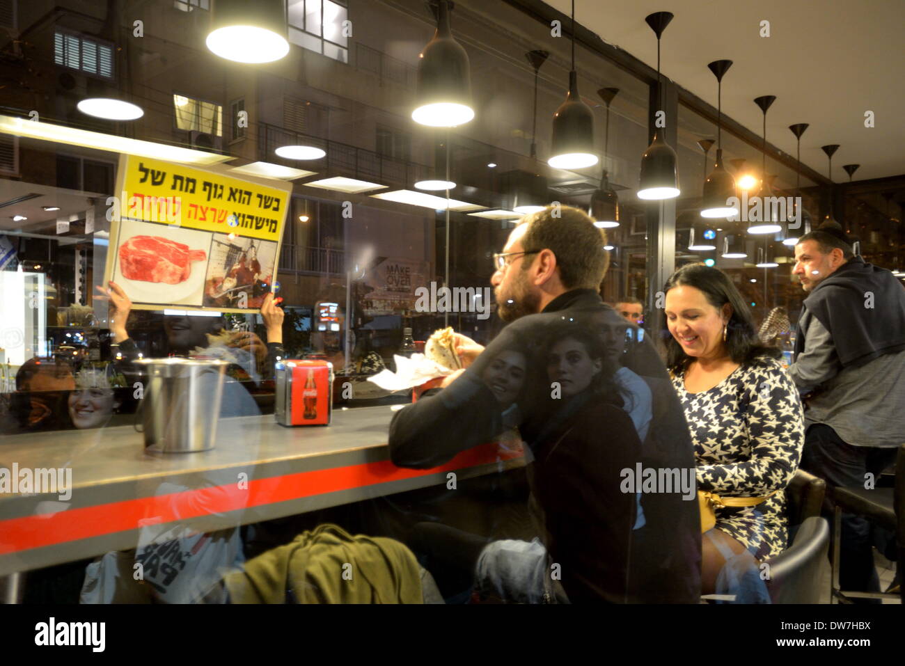 Tel Aviv, Israel. 1. März 2014. TEL AVIV, ISRAEL-MAR 1' St, 2014: Israelis sind Essen in einem Restaurant Fleisch verkaufen, wie ein Tierschützer dagegen einen Banner hält "Fleisch ist ein toter Bod von jemandem Leben wollte" zu lesen. Einige hundert Israelli Tierschützer protestierten in Tel Aviv. Demonstranten aufgerufen, aufhören zu essen und Jagd auf Tiere und für Tierrechte, nicht eingesperrt, versklavt und missbraucht zu kämpfen. Gili Yaari/NurPhoto/ZUMAPRESS.com/Alamy © Live-Nachrichten Stockfoto