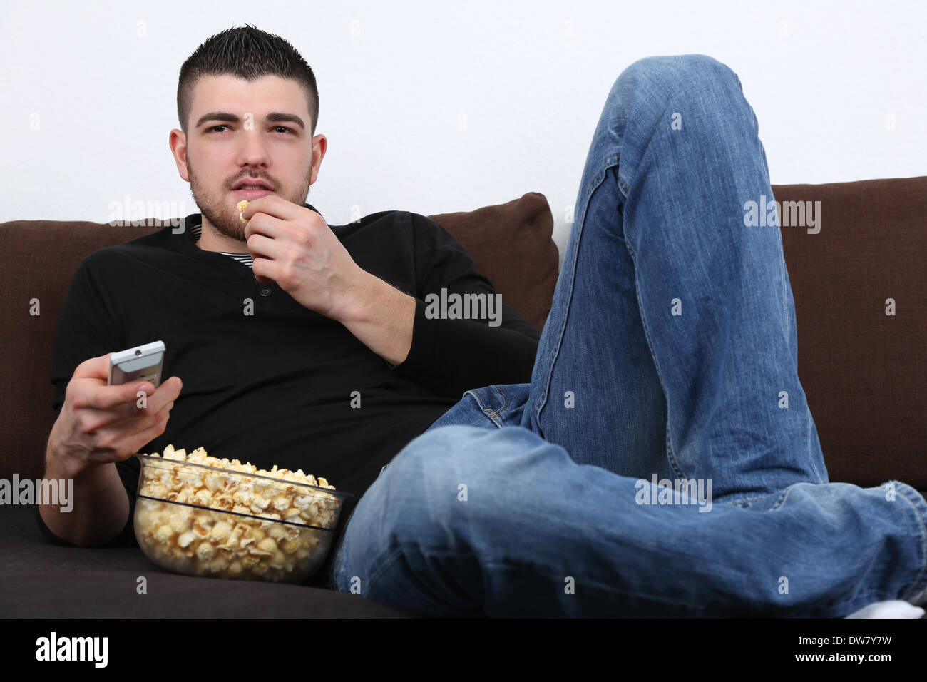 Junger Mann auf einem Sofa liegend, vor dem Fernseher und Essen popcorn Stockfoto