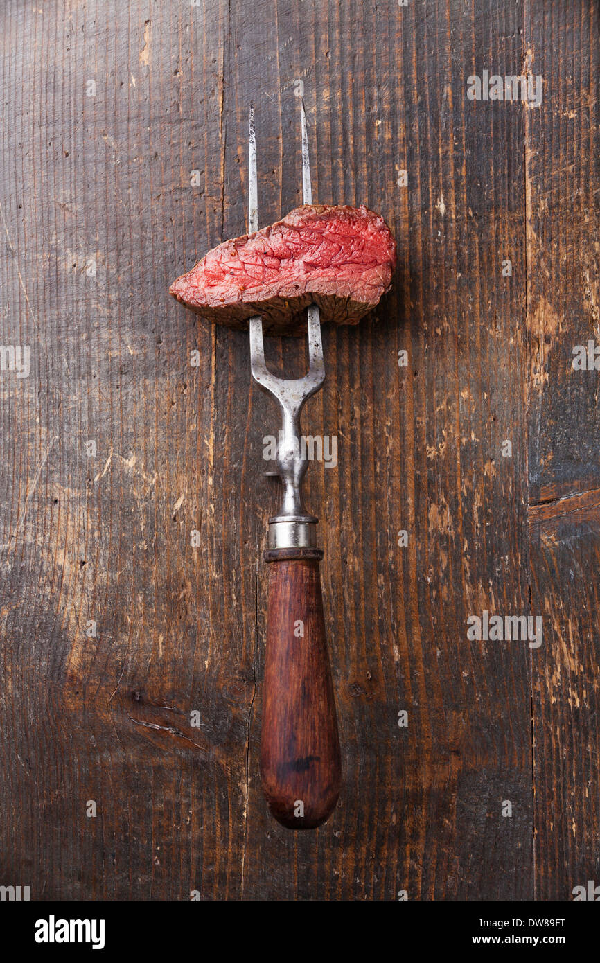 Stück Rindfleischsteak auf Fleischgabel auf hölzernen Hintergrund Stockfoto