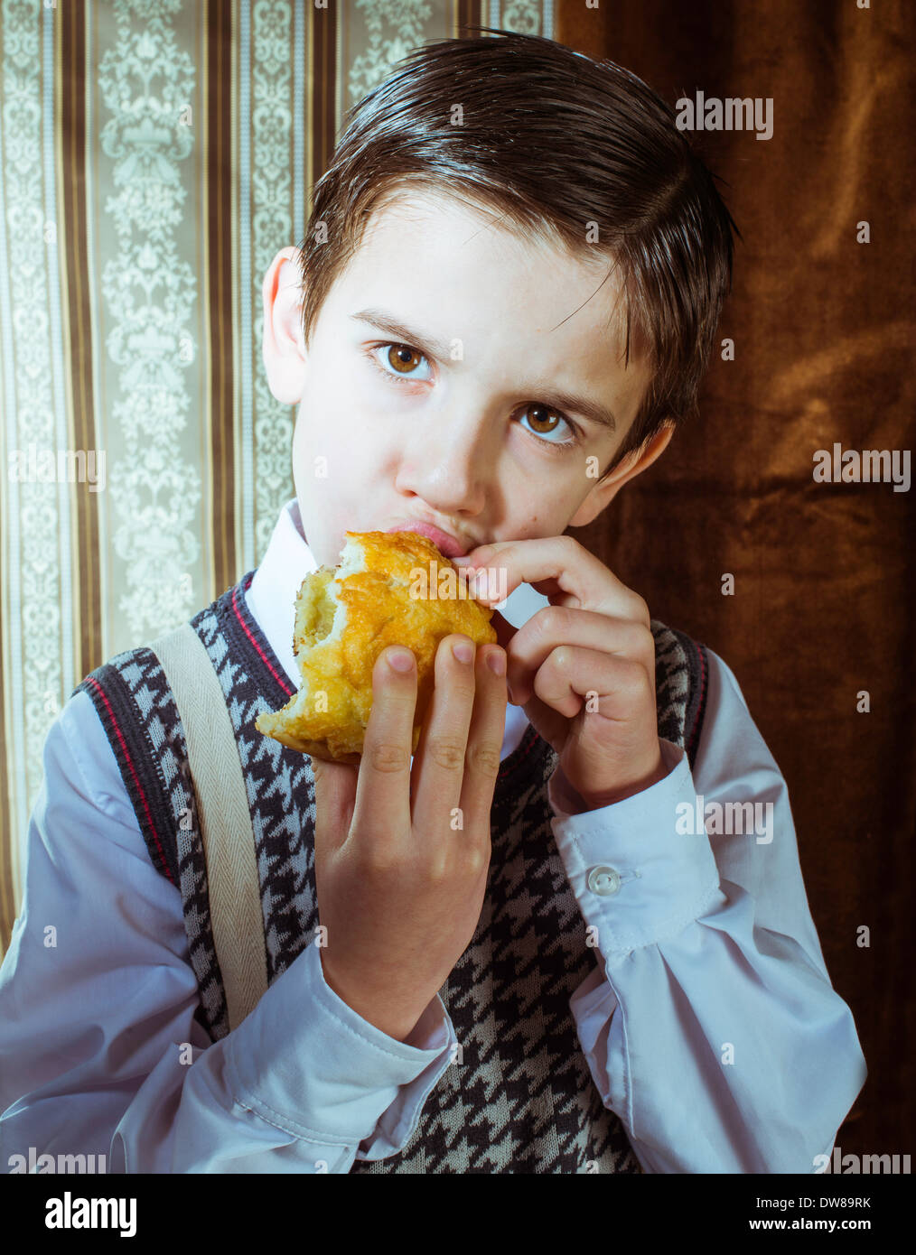 Kind, Krapfen zu essen. Vintage-Kleidung und Hintergrund Stockfoto