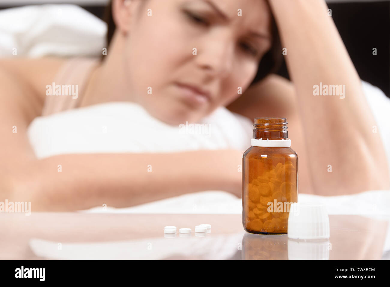 Frau im Bett mit einer Flasche Tabletten vor ihr liegend Stockfoto