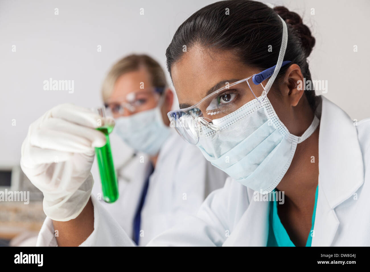 Asiatischen medizinischen oder wissenschaftlichen Forscher oder Frau Ärztin Blick auf ein Reagenzglas grüne Flüssigkeit in einem Labor Stockfoto