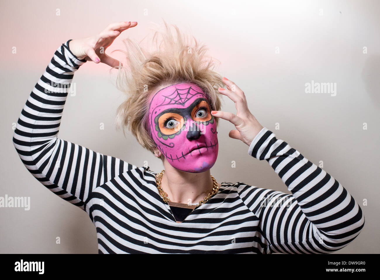 Eine junge Frau mit Zombie Stil Bemalung in rosa und wilden Haaren schlägt eine Horror-Pose für die Kamera. Stockfoto