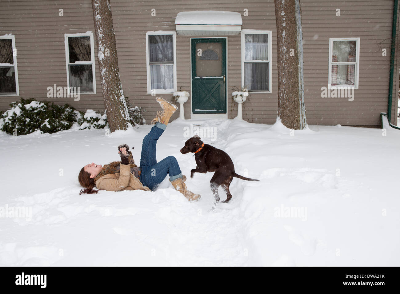 Mitte Erwachsene Frau im Schnee draußen spielen mit Hund Haus liegen Stockfoto
