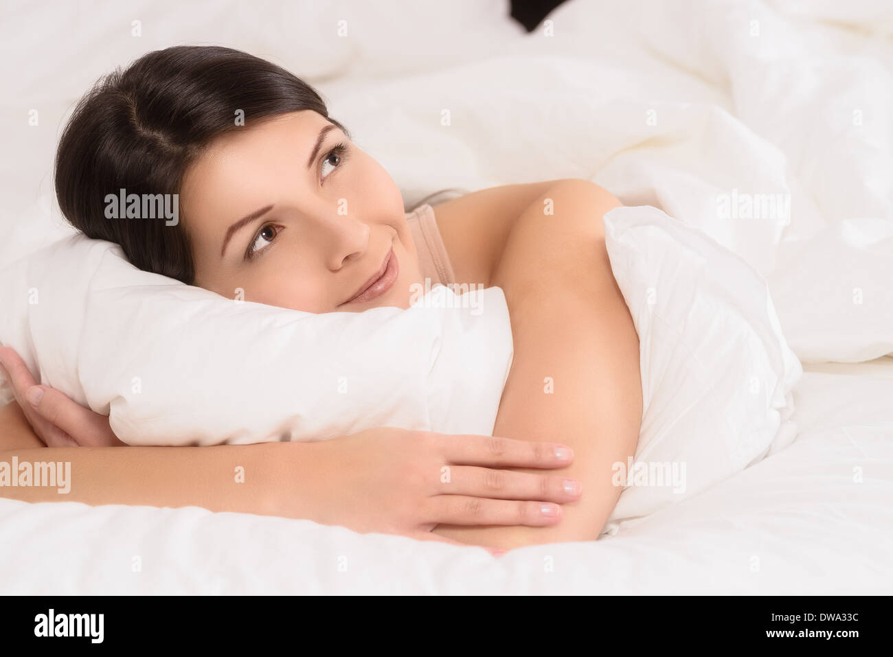 Lächelnde gesunde verjüngt junge Frau kuscheln nach unten zwischen ihre Kissen im Bett, so dass die Kamera eine große Freude strahlend Lächeln Stockfoto