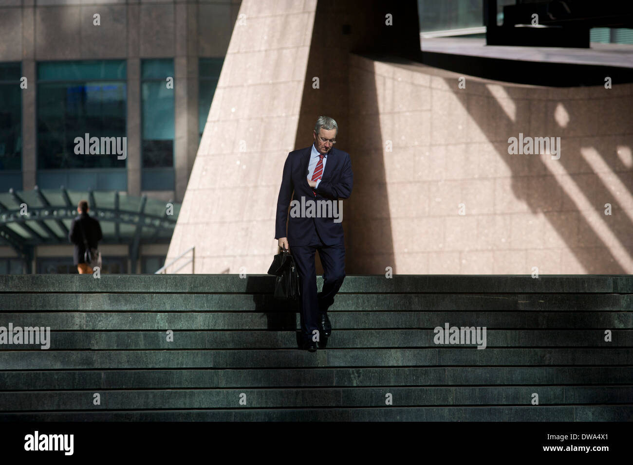 Geschäftsmann, ein Spaziergang durch die Broadgate Firmensitze Entwicklung in der City of London. Fuß Schritte auf seinem Weg nach oder von einem Termin oder eine Besprechung, prüft der Mann eine innere Tasche wie er seinen Weg zu einem Raum der reflektiertes Sonnenlicht mit dem Hintergrund der Broadgate Entwicklung innerhalb der alten Grenzen der Hauptstadt Square Mile macht, es ist Bankenviertel von den Römern in AD43 gegründet. Stockfoto
