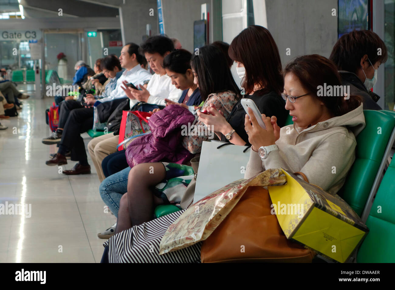 Reisende, die auf ihren Smartphones in der Passagier-Terminal des Flughafen Suvarnabhumi, Bangkok, Thailand. Stockfoto