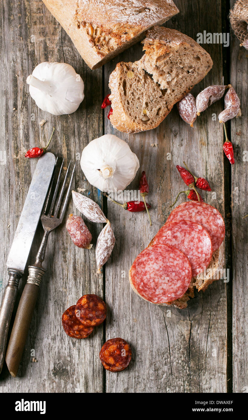 Wenig Salami mit Rot-heiße Paprika, Knoblauch und frischem Brot über alten Holztisch. Stockfoto