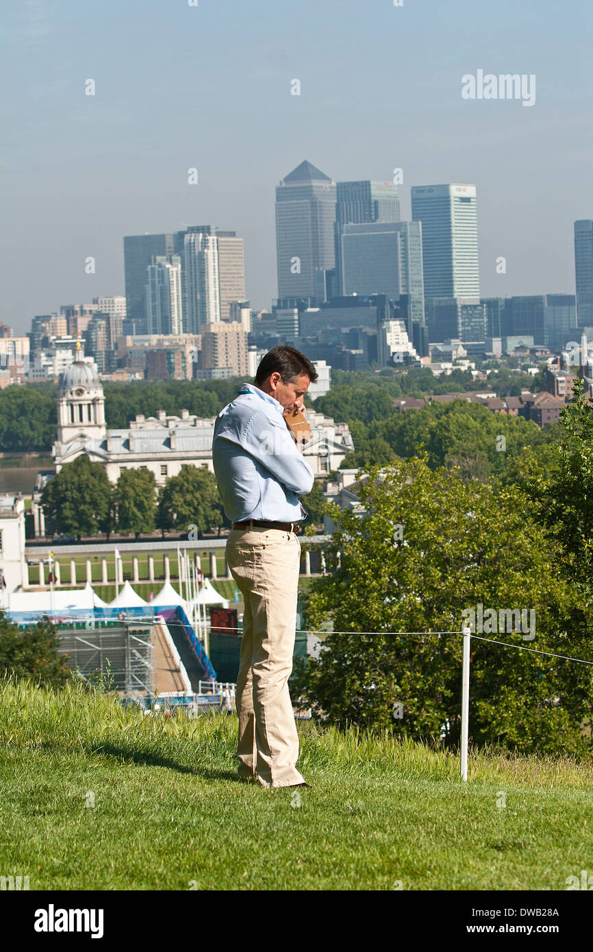 Lord Coe am Telefon durch das Royal Observatory in Greenwich mit Canary Wharf im Hintergrund Stockfoto