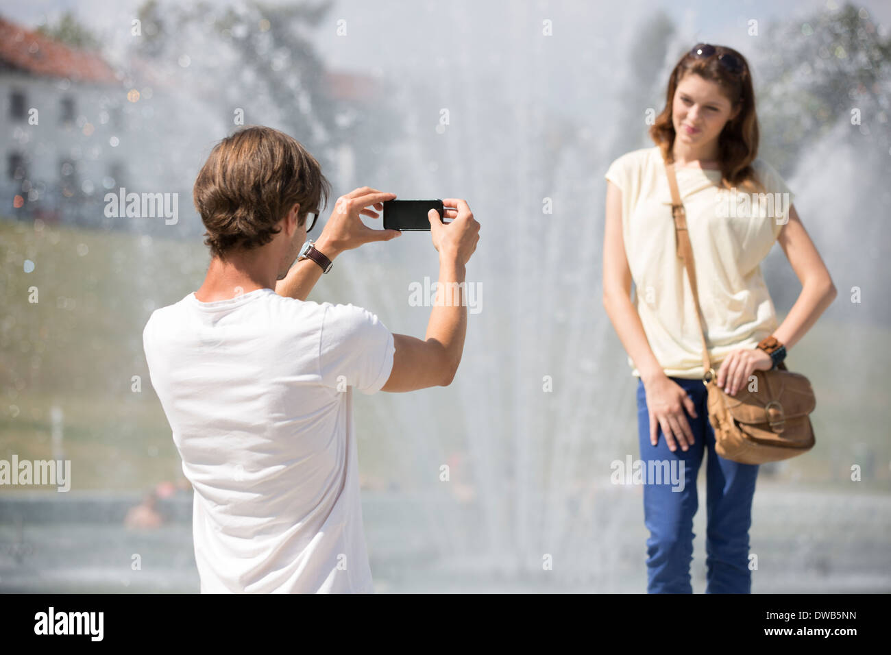 Junger Mann fotografiert Frau gegen Brunnen Stockfoto