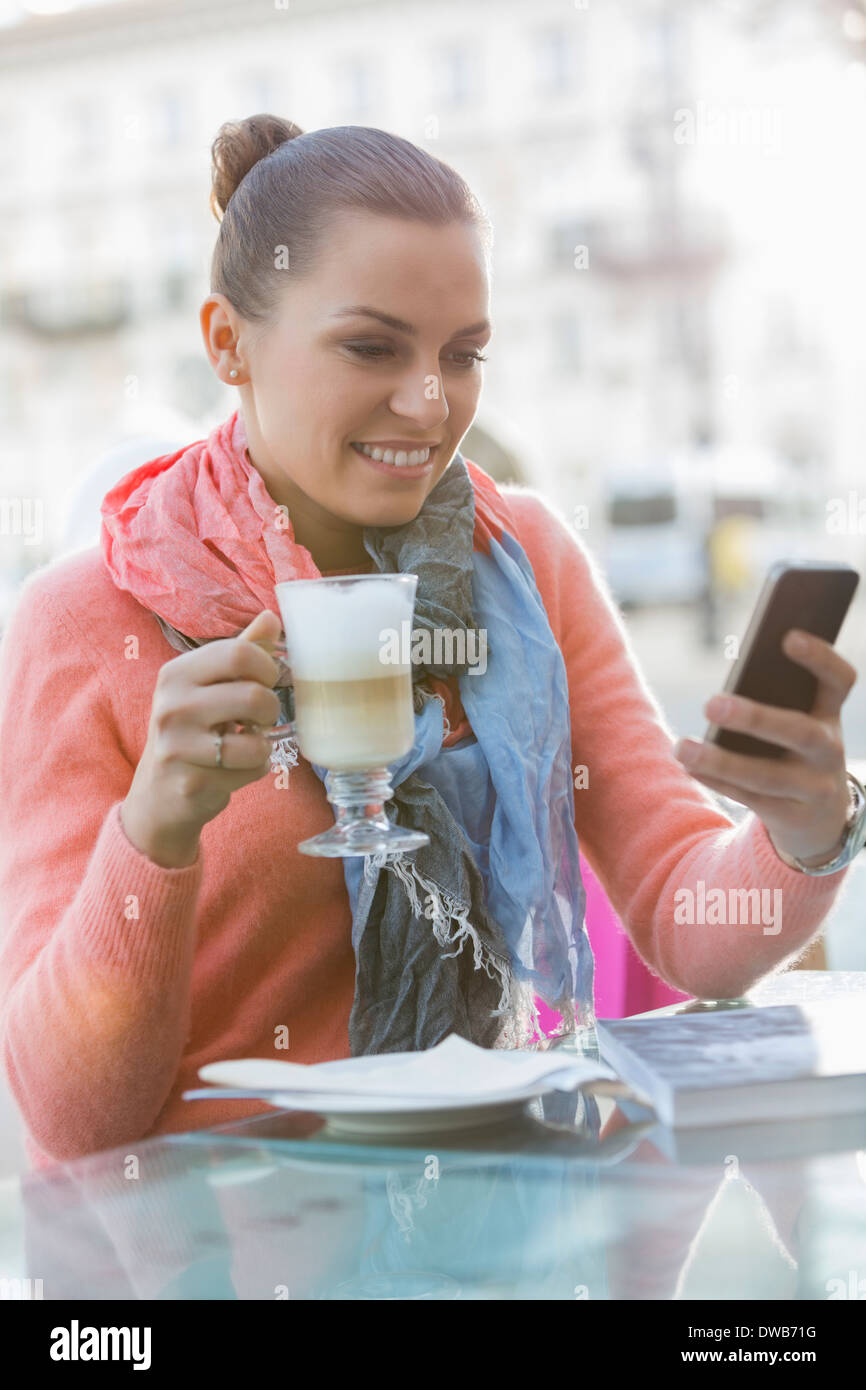 Junge Frau mit Kaffee zwar mit Handy im Straßencafé Stockfoto