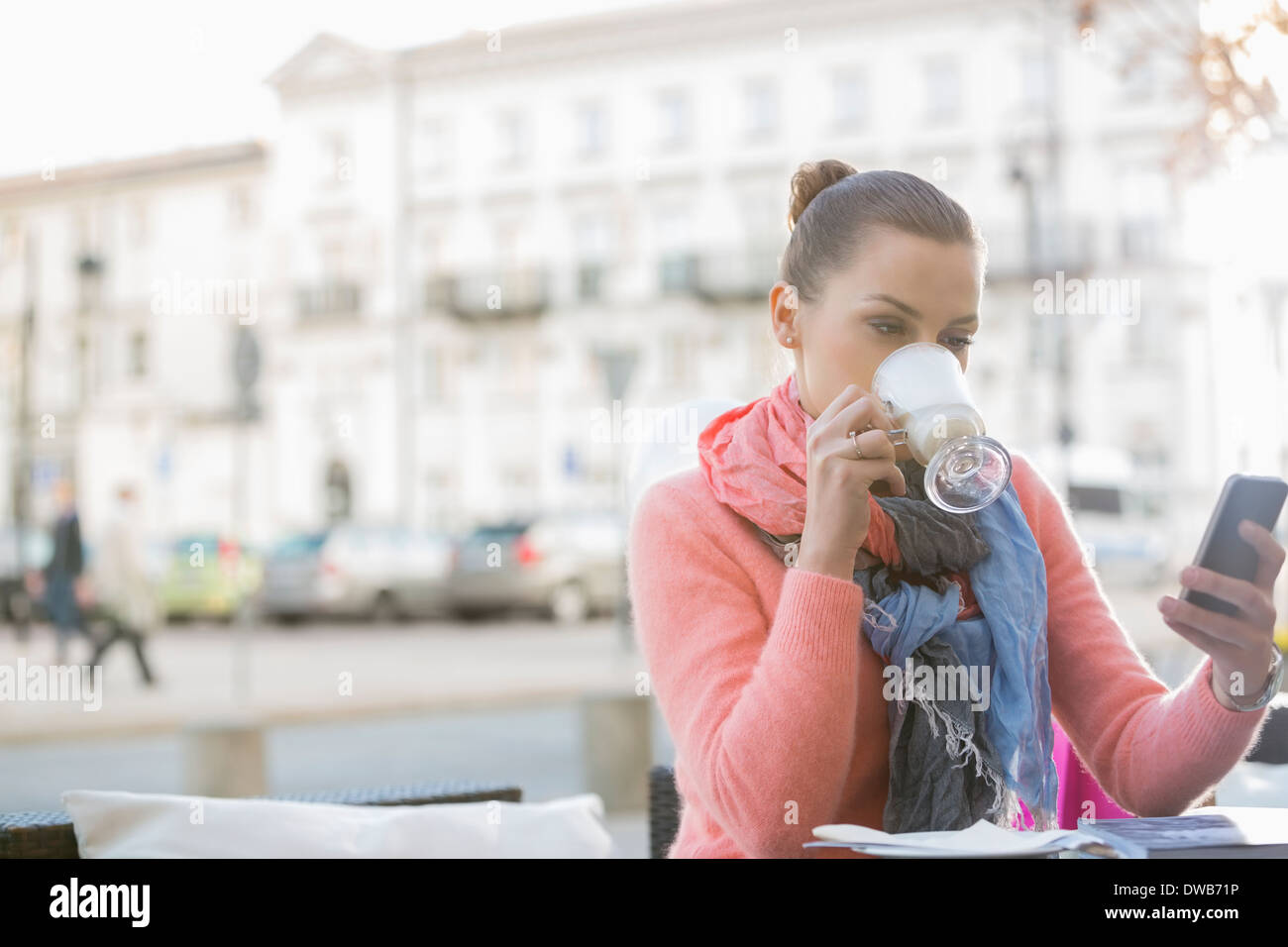 Junge Frau Kaffee trinken, während mit Handy im Straßencafé Stockfoto