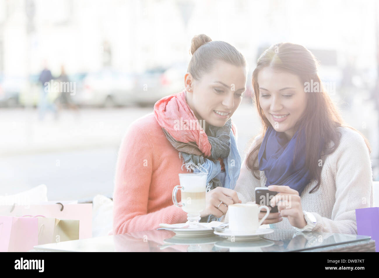 Glückliche Frauen mit Handy im Straßencafé im winter Stockfoto