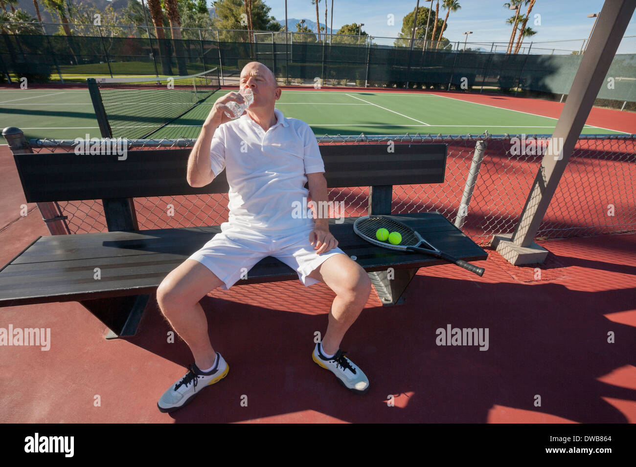 Senior männlichen Tennis Spieler Trinkwasser während Sie gemütlich auf Gericht Stockfoto