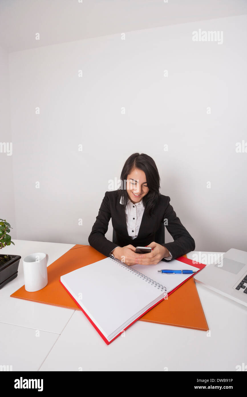 Geschäftsfrau-SMS über Handy am Schreibtisch Stockfoto
