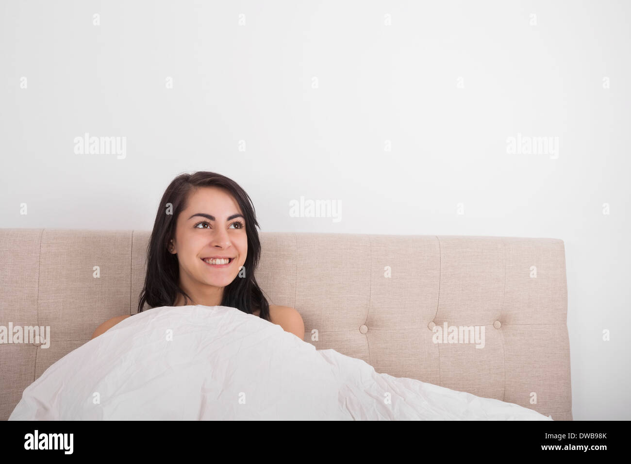 Nachdenkliche junge Frau lächelnd im Bett Stockfoto
