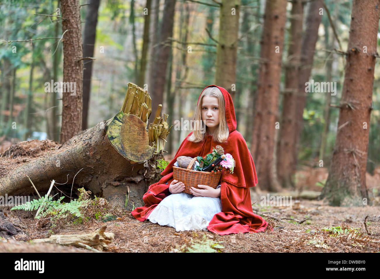 Mädchen-Maskerade als Red Riding Hood sitzen auf dem Boden im Wald Stockfoto