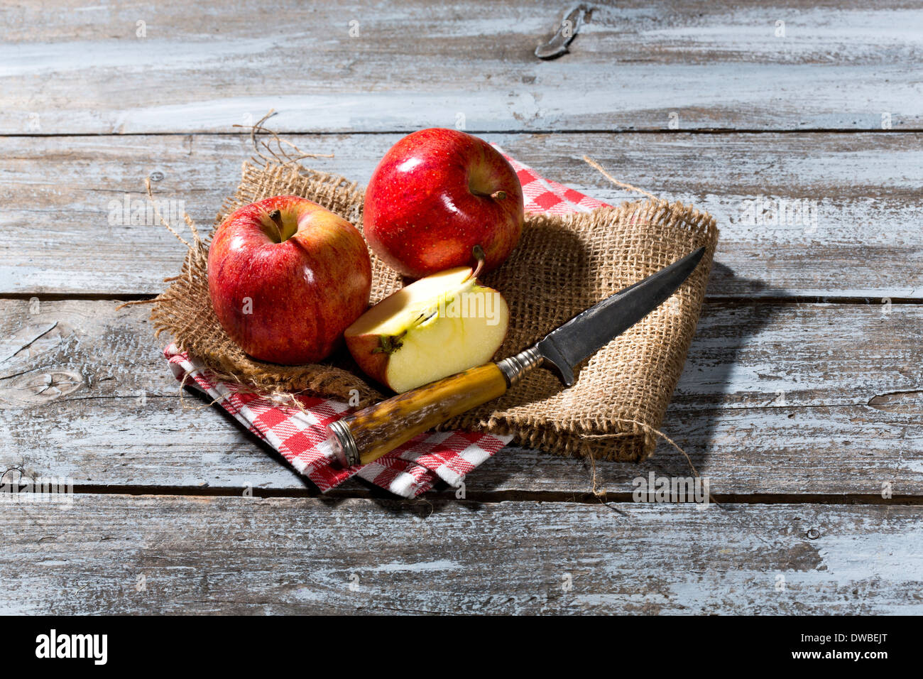 In Scheiben geschnitten und ganz rote Äpfel und Messer auf Jute, Stoffserviette und Holztisch Stockfoto