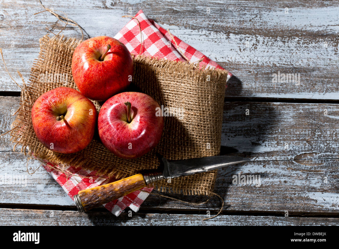 Drei rote Äpfel und Messer auf Jute, Stoffserviette und Holztisch Stockfoto