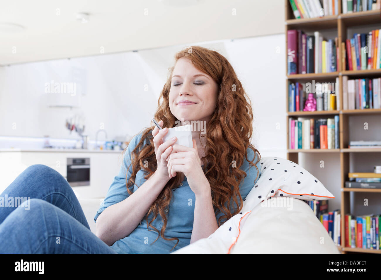 Junge Frau sitzt auf der Couch halten Tasse Kaffee Stockfoto