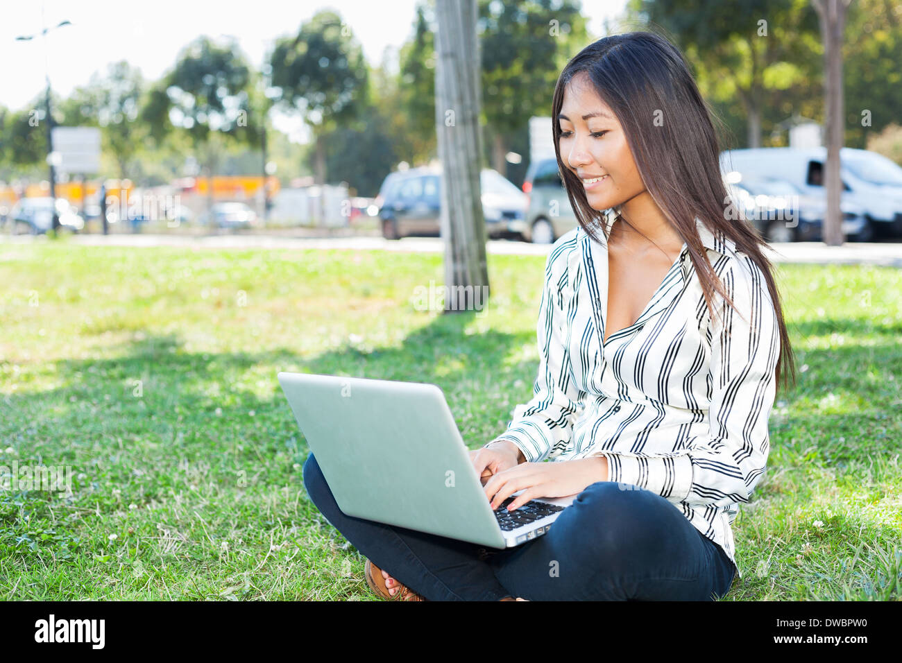Lächelnd Asiatin mit einem Laptop sitzen auf dem Rasen Stockfoto