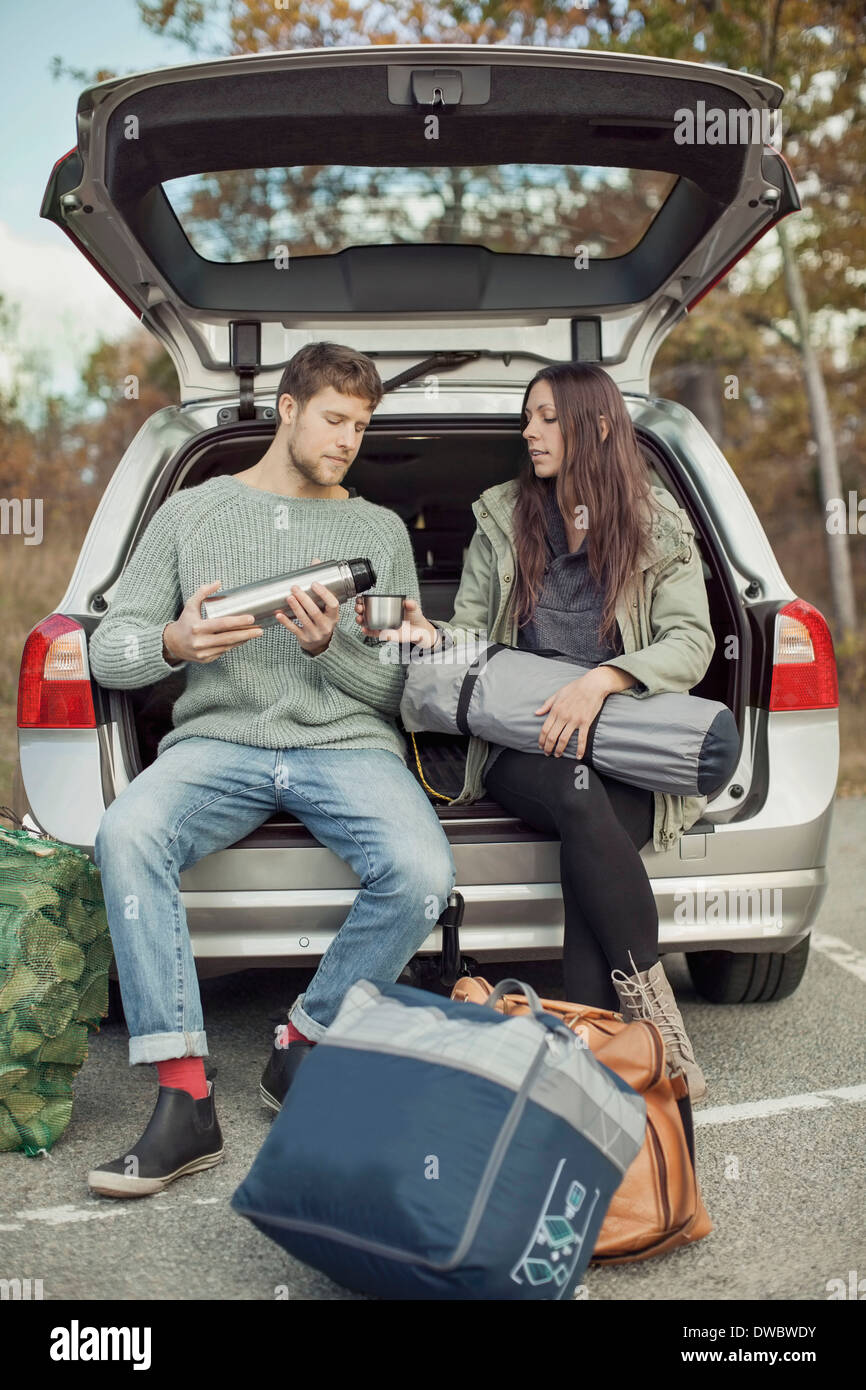 Man gießt Kaffee für Frau sitzend im Kofferraum eines Autos beim camping Stockfoto