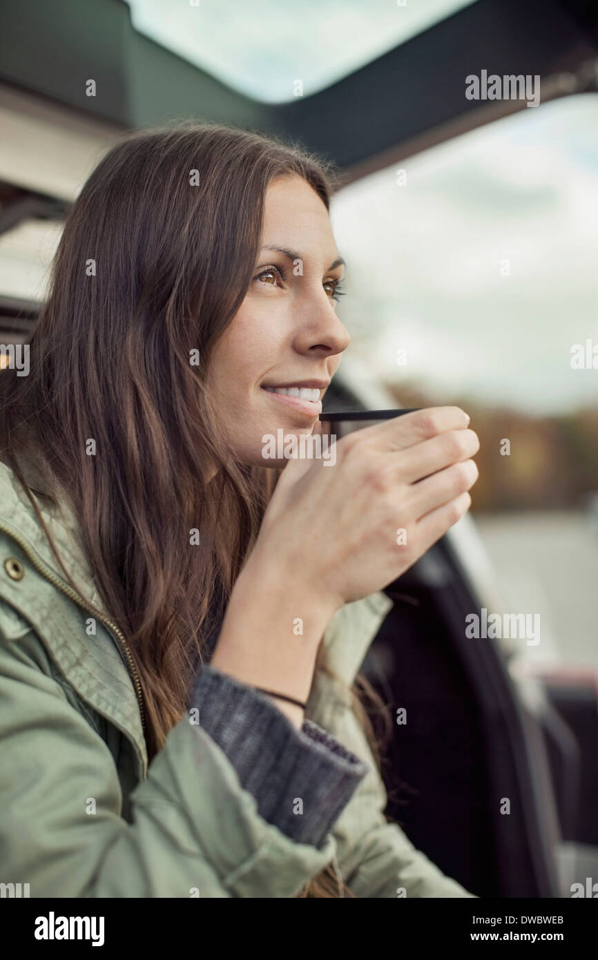 Junge Frau beim Kaffeetrinken im Kofferraum eines Autos die wegsehen Stockfoto