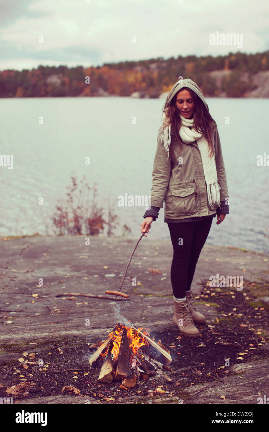Voller Länge Frau Kochen Wurst in Lagerfeuer am Seeufer Stockfoto