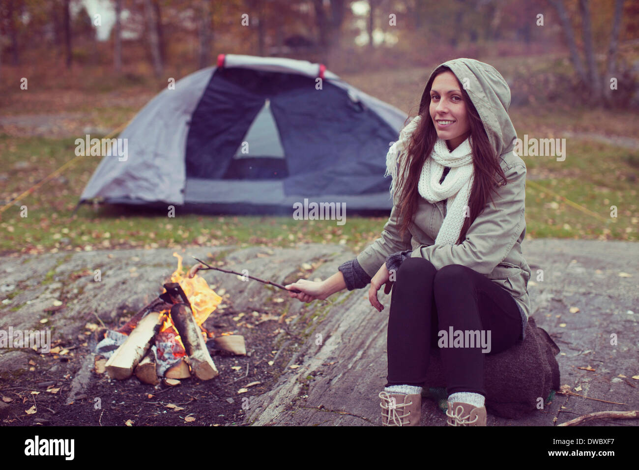 Porträt der Frau Kochen Wurst in Lagerfeuer gegen Zelt im Wald Stockfoto