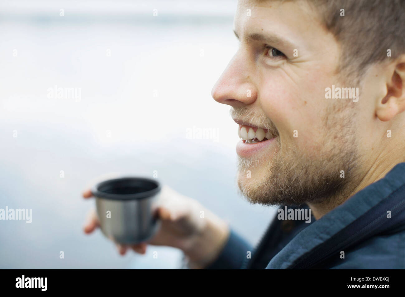 Glücklicher Mann halten Kaffeetasse gegen See Stockfoto