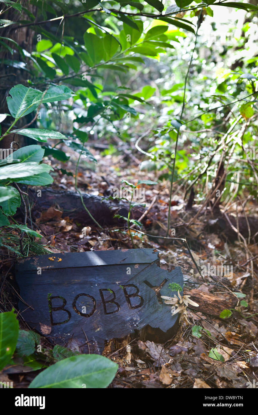 Ein Tierfriedhof im Wald, mit einem Baumstamm Grabstein mit Haustiere Namen eingeschrieben. Stockfoto
