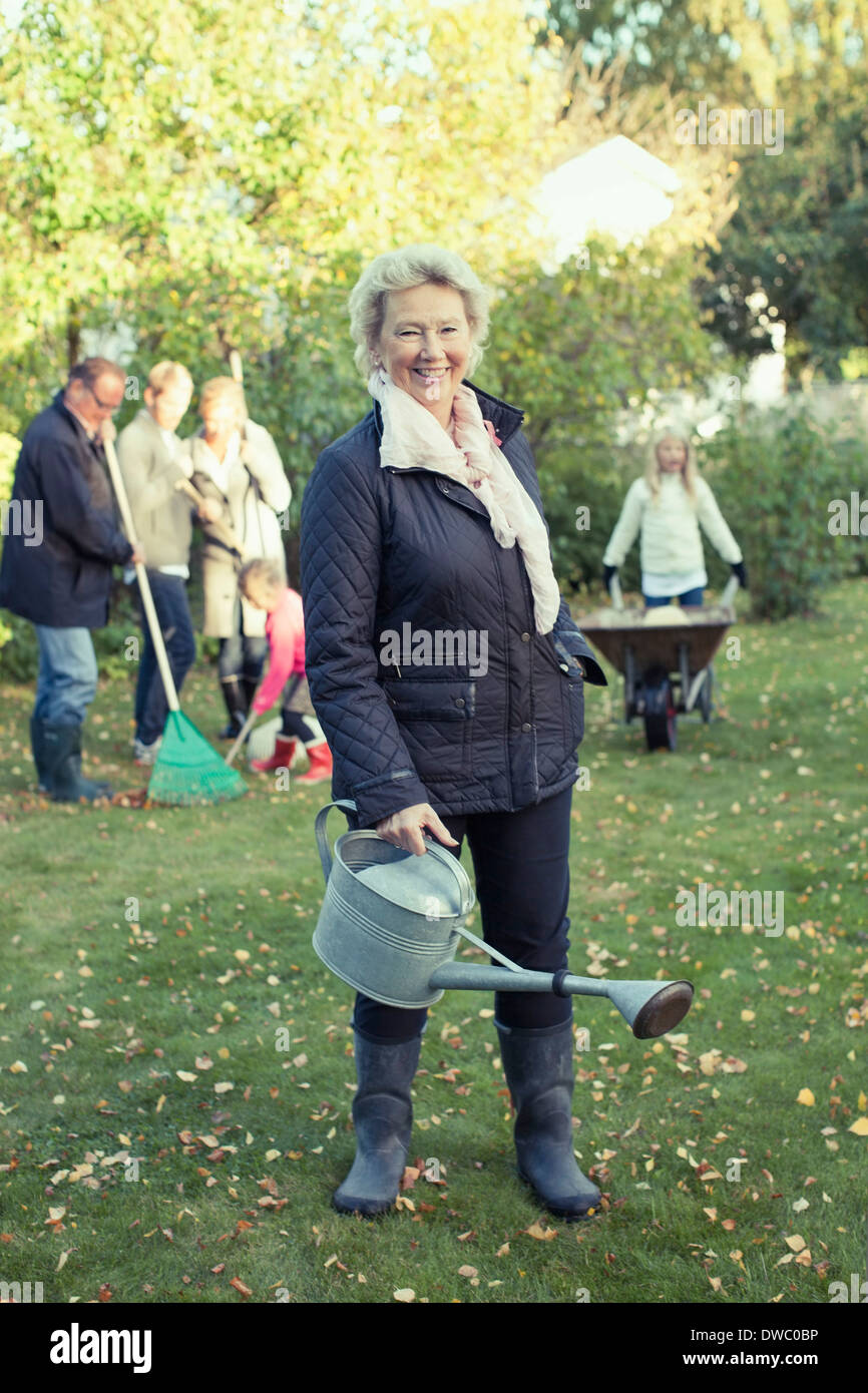 Porträt der älteren Frau, die Gießkanne bei der Gartenarbeit mit Familie am Hof Stockfoto