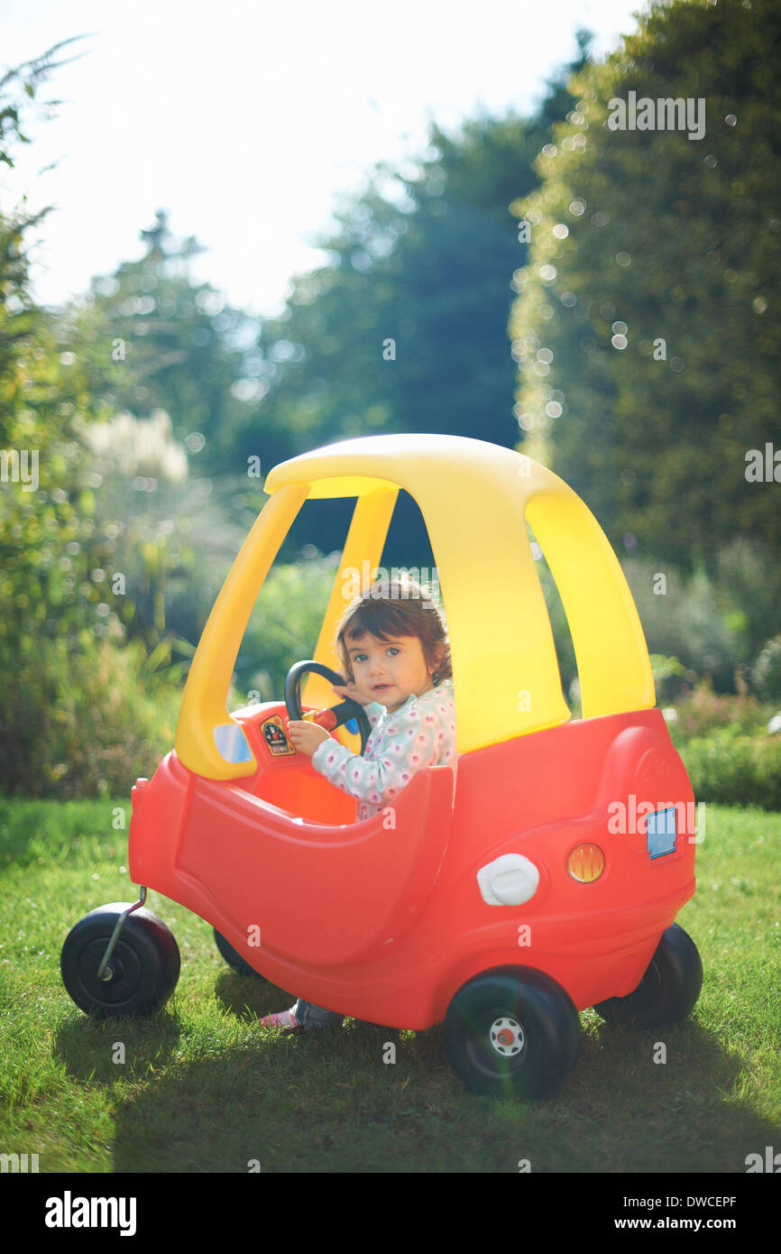 Weiblichen Kleinkind im Spielzeugauto im Garten spielen Stockfoto