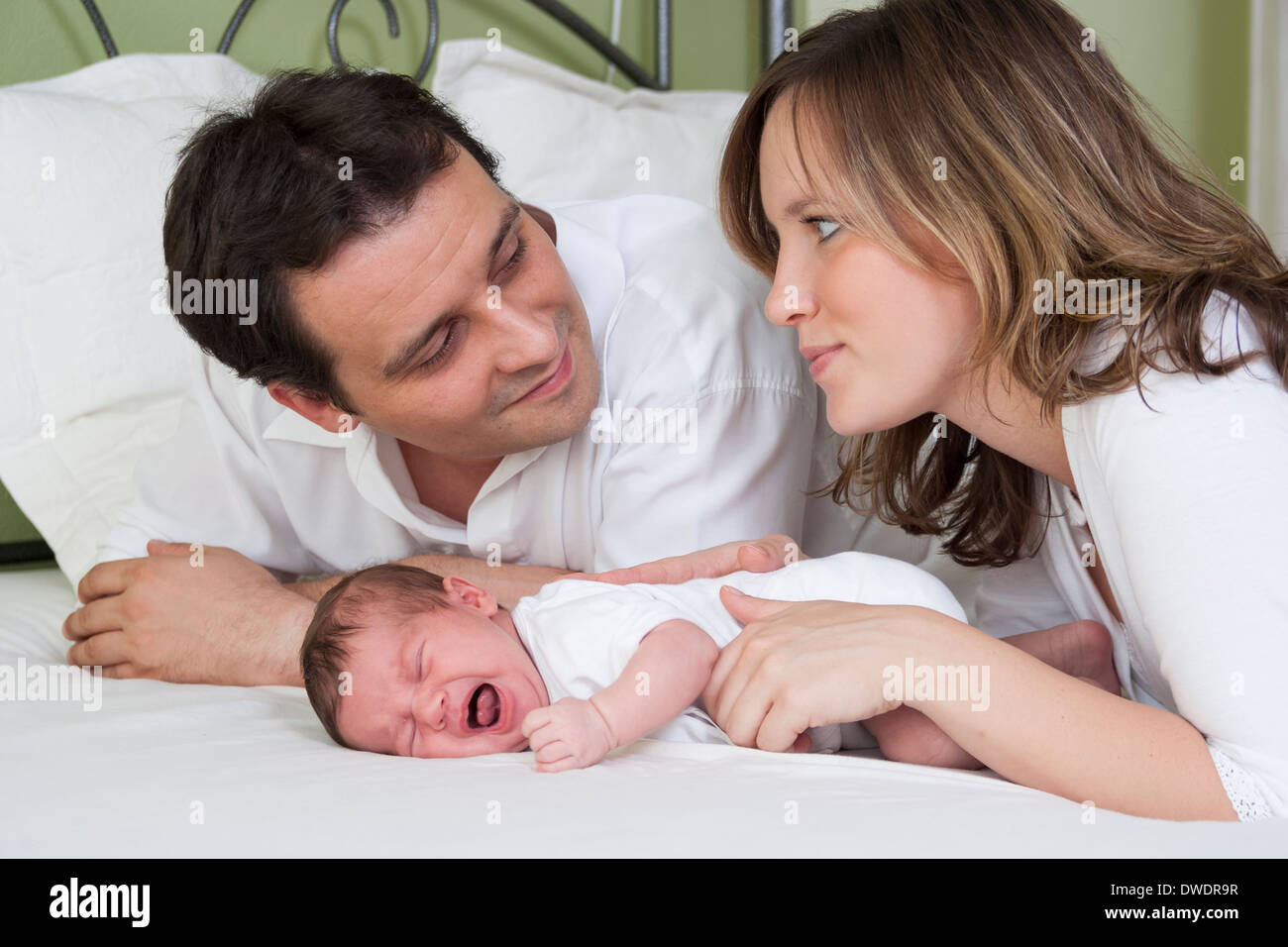 Eltern mit Neugeborenen Mädchen auf Bett liegend Stockfoto