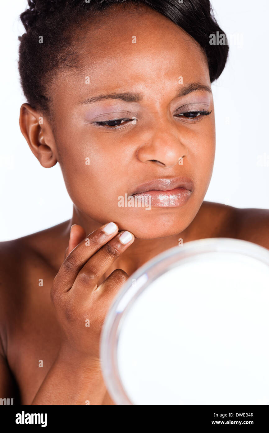 Junge afrikanische Frau im Studio tun, Körperpflege und überprüfen ihr Gesicht für Pickel und Flecken mit Spiegel für Jung und schön Stockfoto