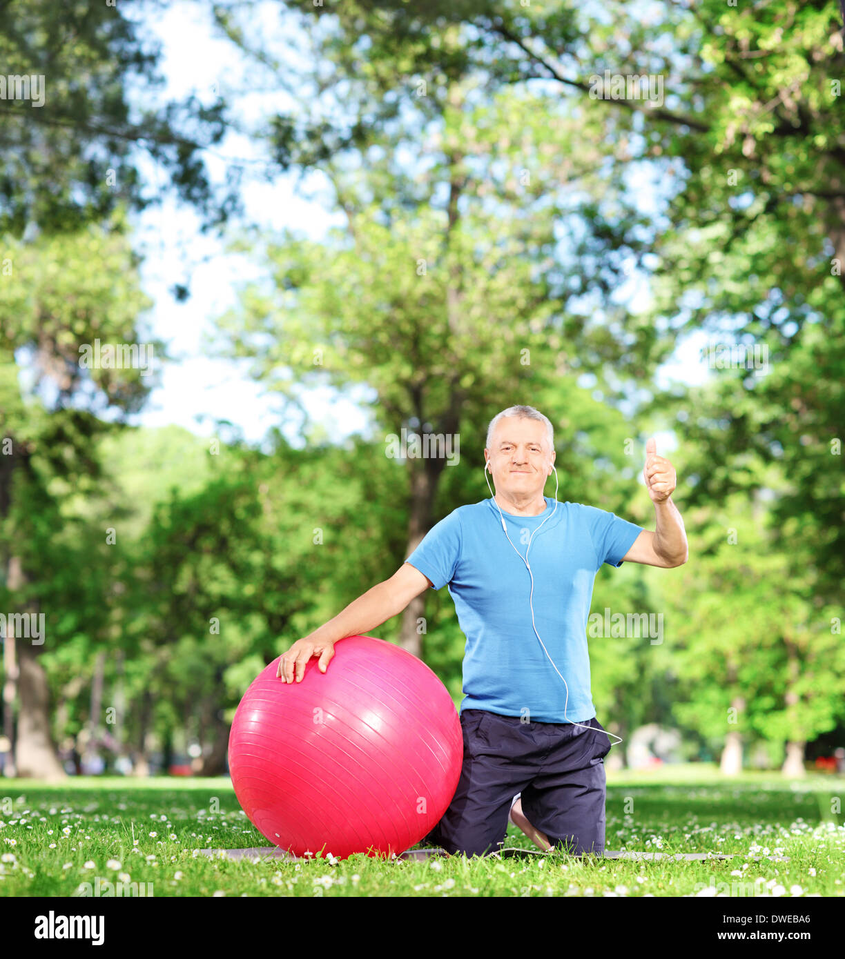 Mann in der Sportswear sitzen auf einer Matte im Park trainieren und Daumen aufgeben Stockfoto