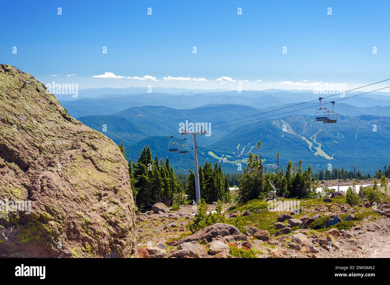 Sessellift hinauf Mount Hood mit Wald bedeckt, Hügel im Hintergrund und einem großen Felsbrocken im Vordergrund Stockfoto