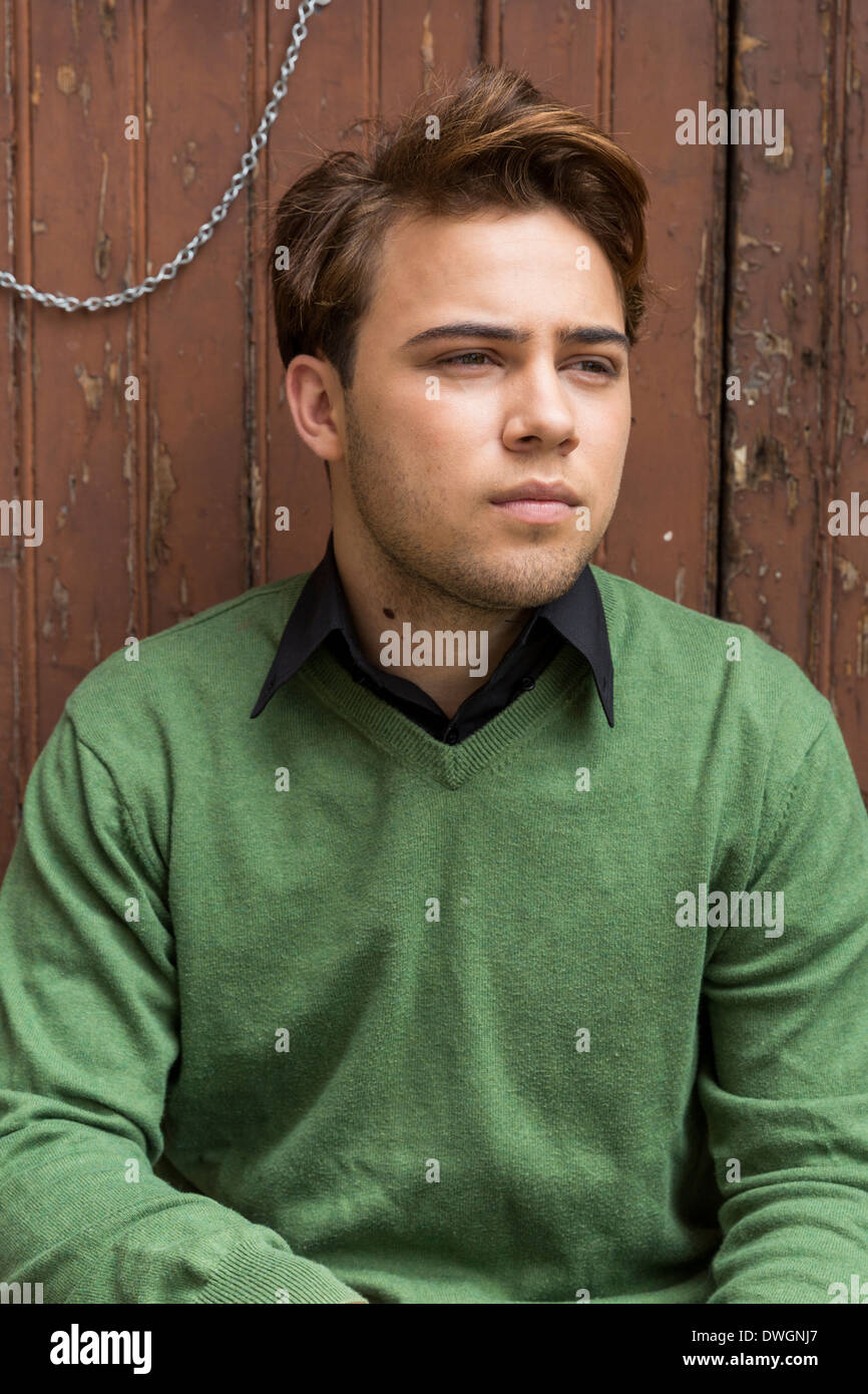 Gut gekleidete junge Mann sitzen gegen eine braune Holz Tür Stockfoto