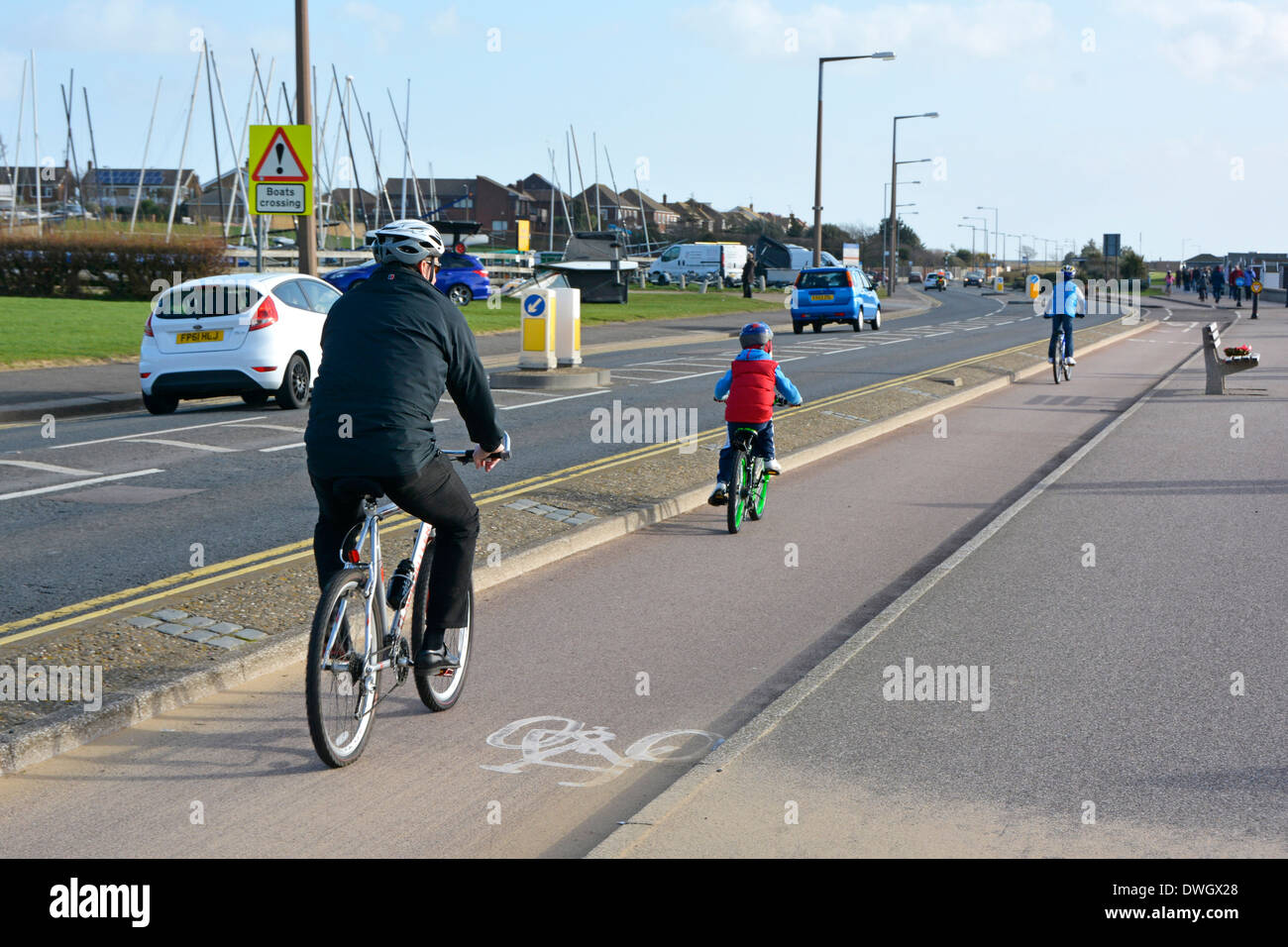 Vater und Sohn, sonnige Radfahrer im Winter, auf einer speziellen Fahrradspur am Straßenrand neben dem Verkehr am Meer in Southend auf der Sea Essex England UK Stockfoto
