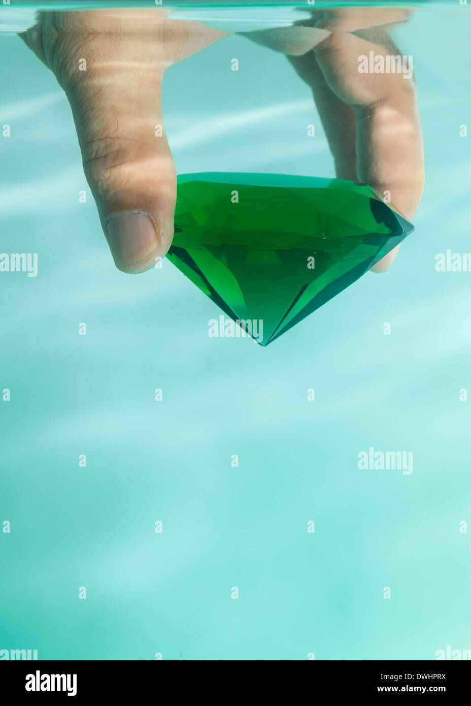 Hand, die eine grünen Smaragd gegen einen hellgrünen Hintergrund Stockfoto