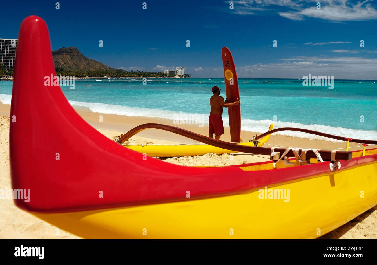 Ausleger-Kanu und Surfer mit einem Surfbrett am Strand von Waikiki, Hawaii, USA. Stockfoto