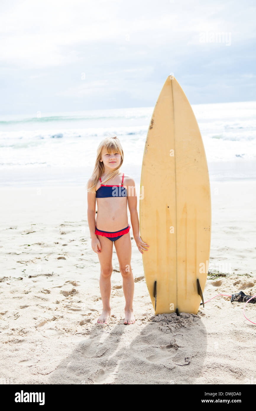 Süße junge Mädchen stehen neben Surfbrett am Strand mit Meer im Hintergrund Stockfoto