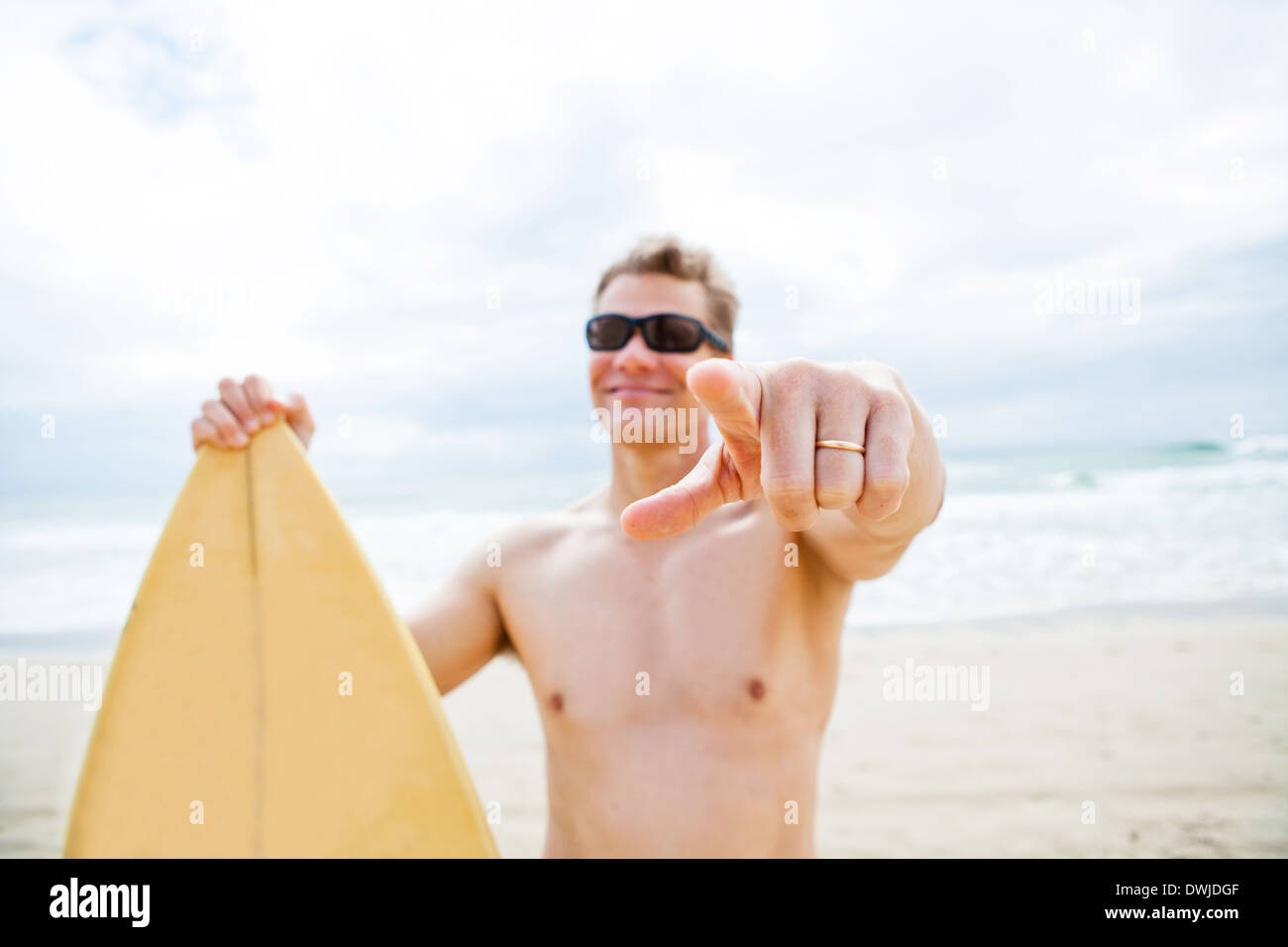 Zeigefinger der verheirateten lächelnd männliche Surfer mit Surfbrett am Strand im Fokus Stockfoto