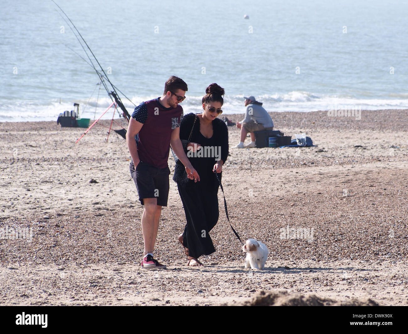 Ein paar, die ihren Hund spazieren gehen, am Strand von Eastney in Portsmouth, Hampshire Stockfoto