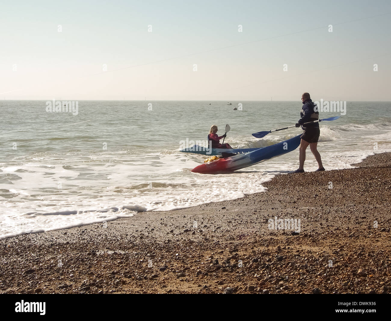 ein Mann zieht ein Meer Kajak aus dem Wasser und an einem Strand Stockfoto